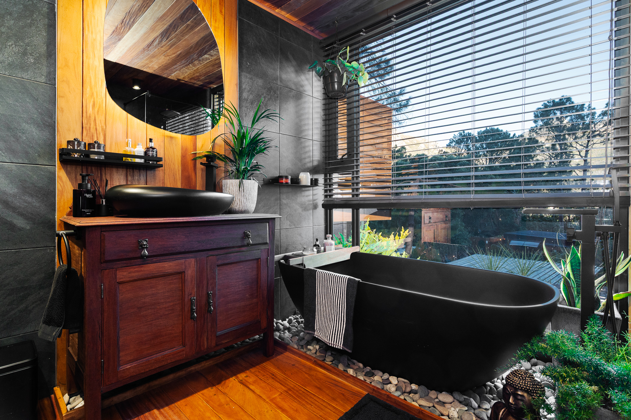 Bathroom with a matte black freestanding bath on river pebbles beside a large window