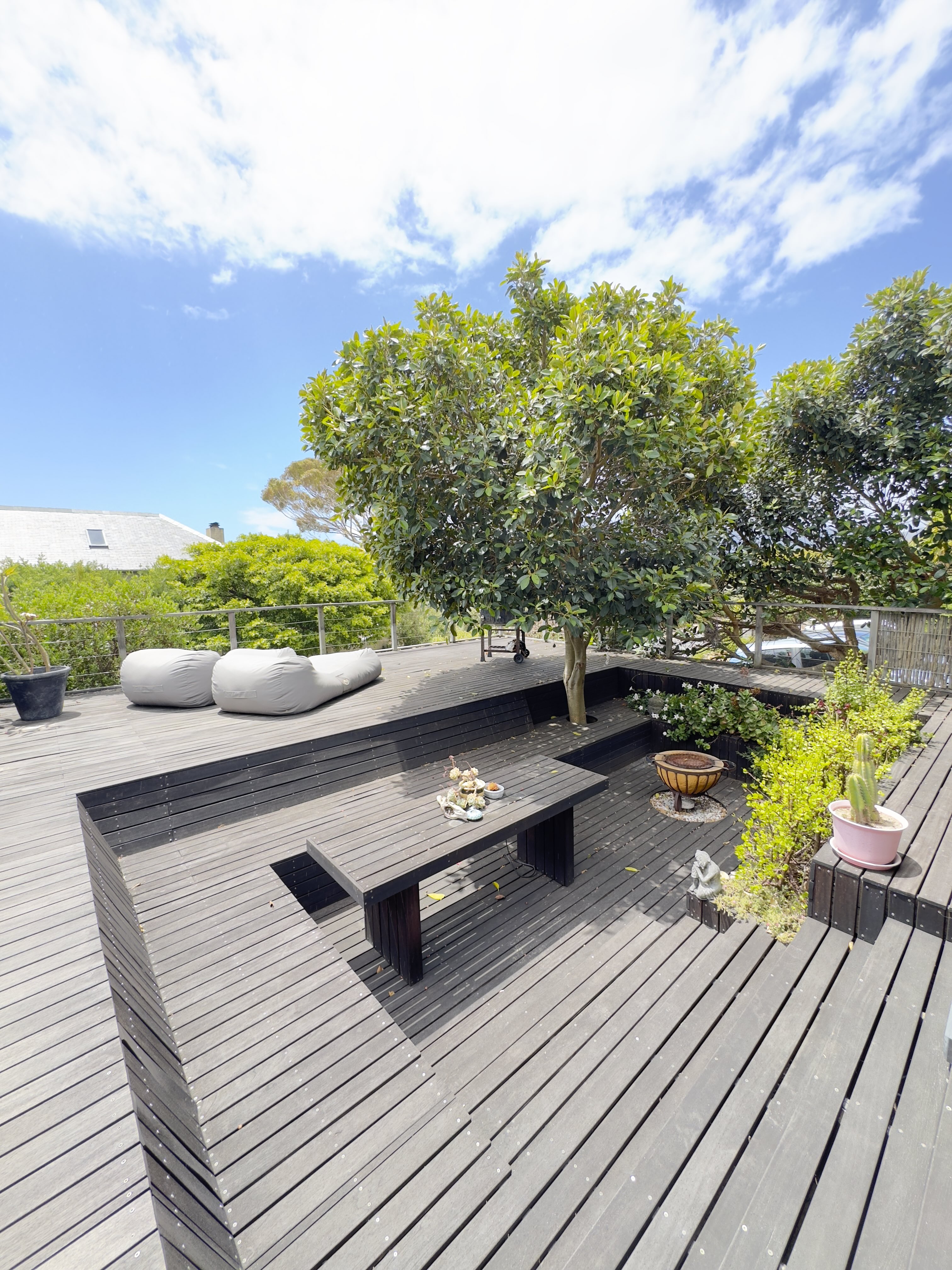 An elevated timber deck wrapping a mature tree with built in benches, a fire bowl and garden views