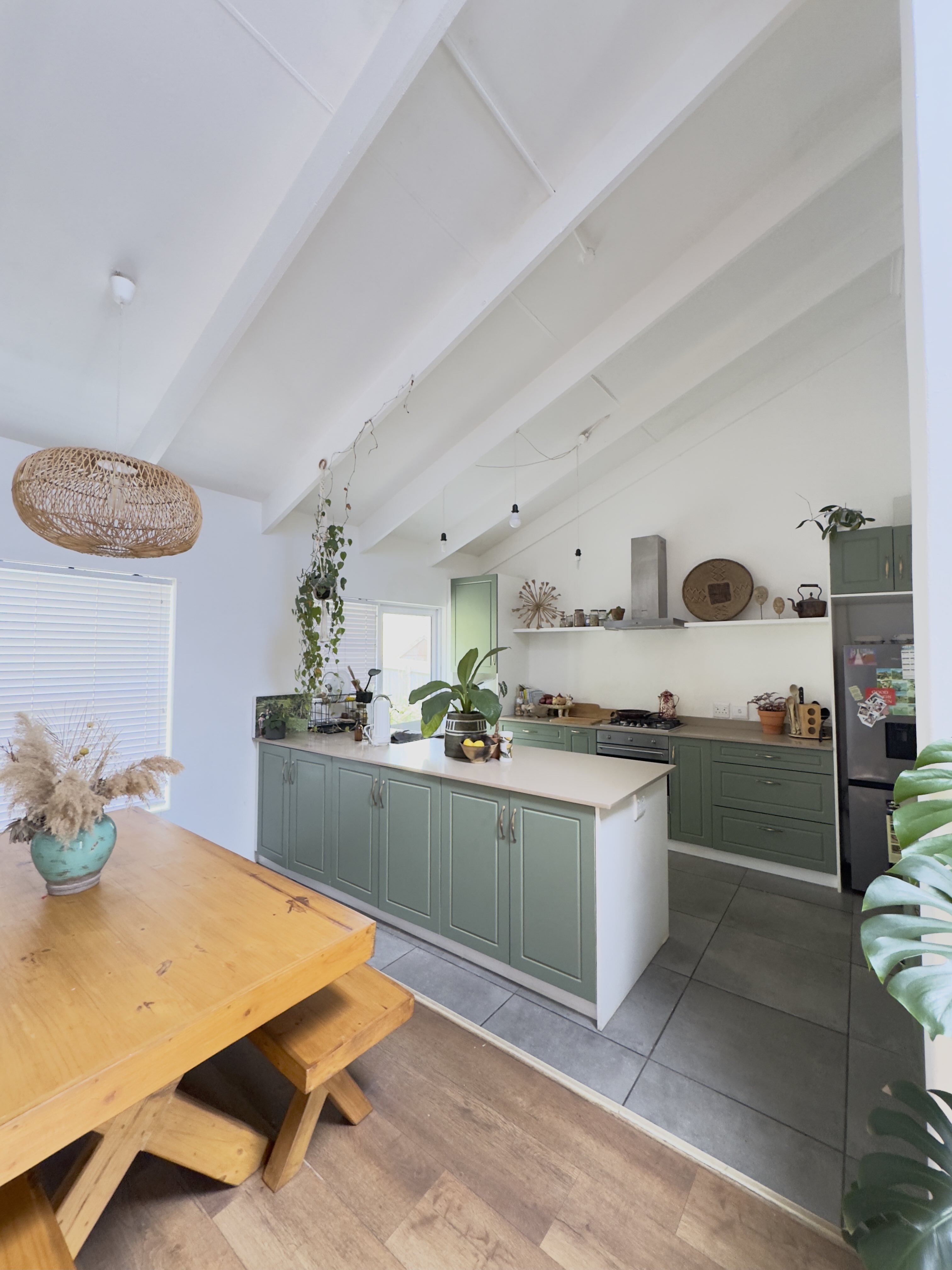 The extended open plan kitchen with sage green cabinetry under the white vaulted ceiling and a timber dining table