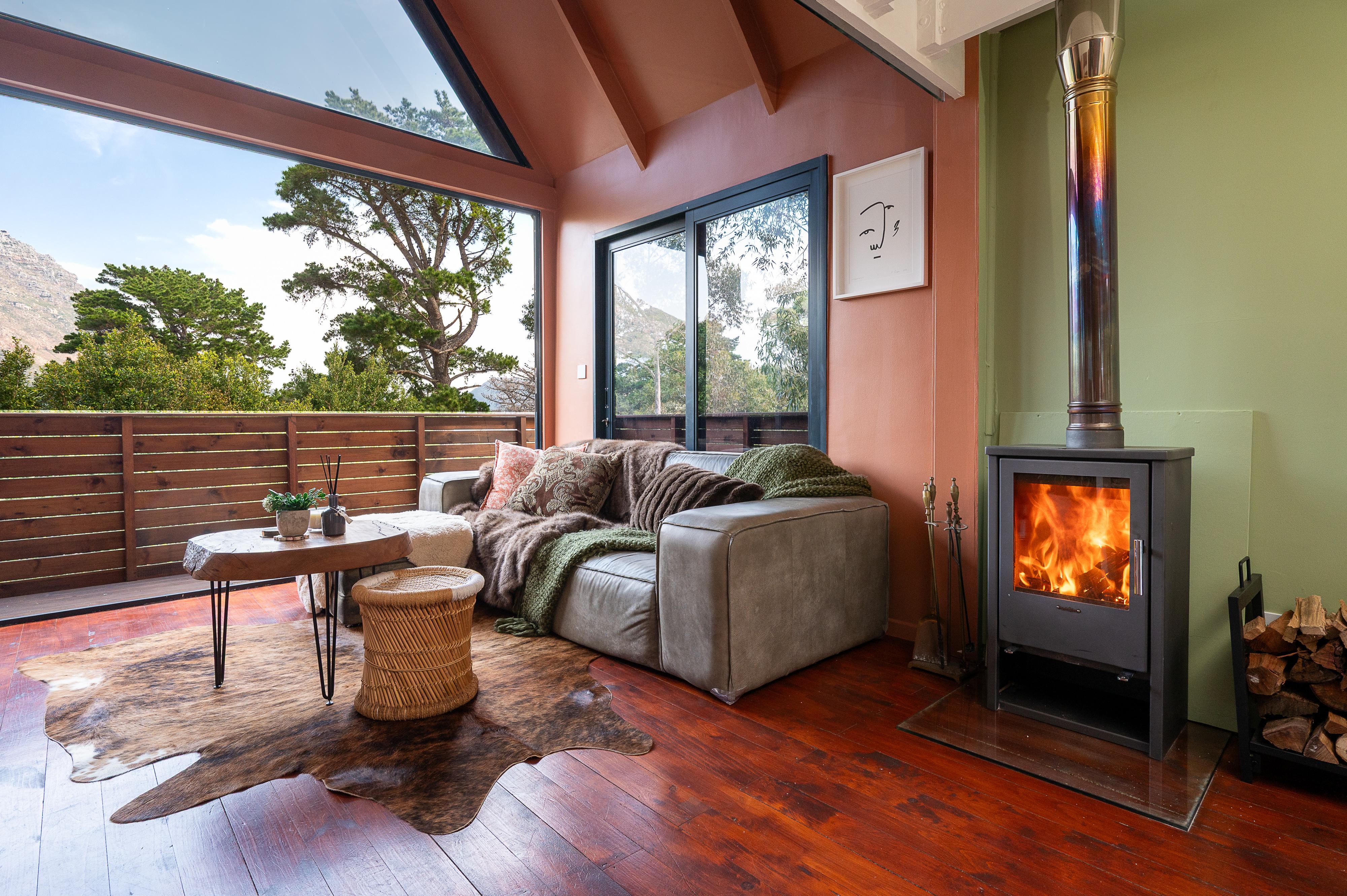 Living room with a wood burning stove and large glass doors opening to a forest view