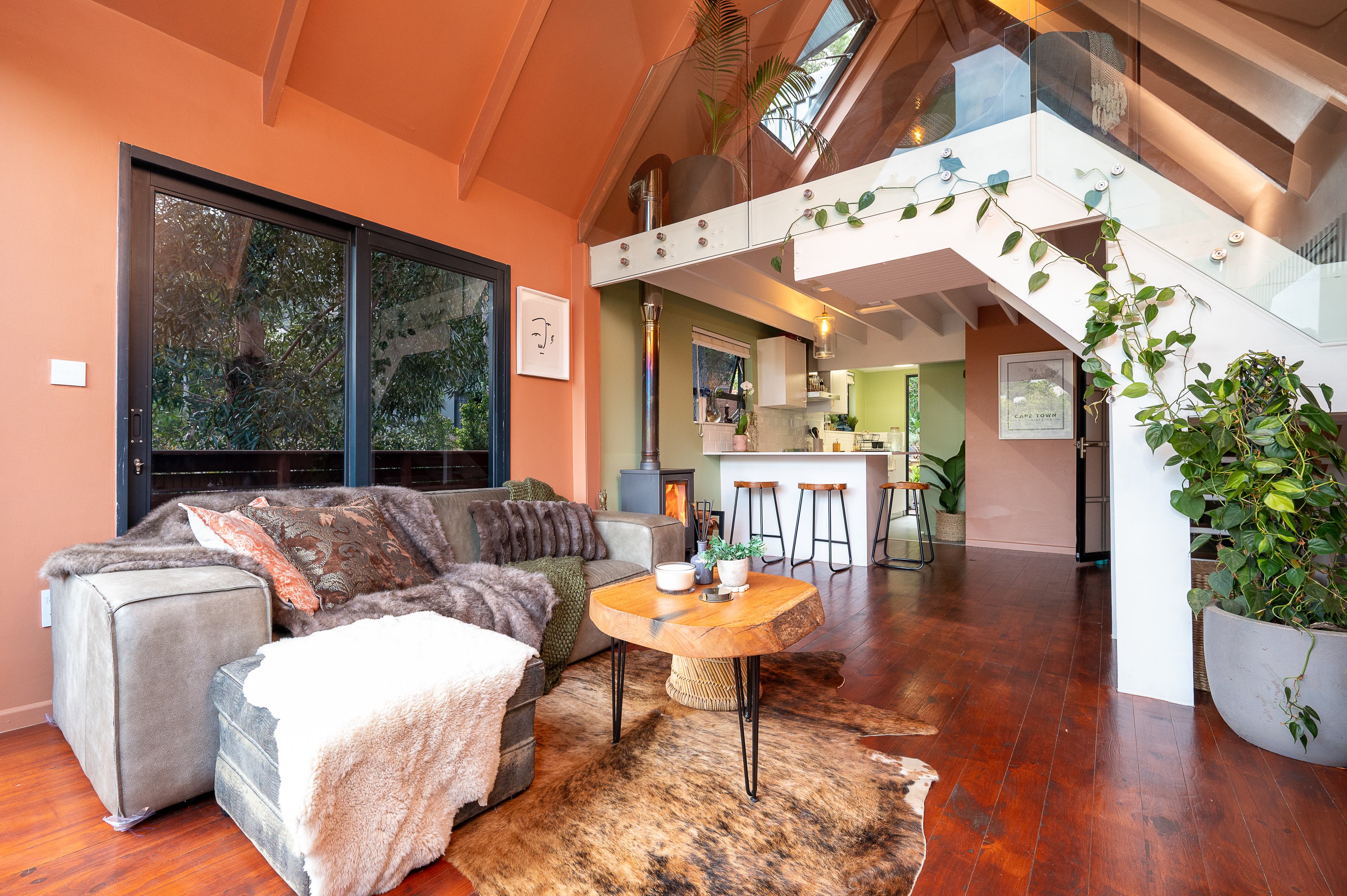 Lounge and kitchen with reclaimed timber floors, wood stove and a glass balustraded loft above