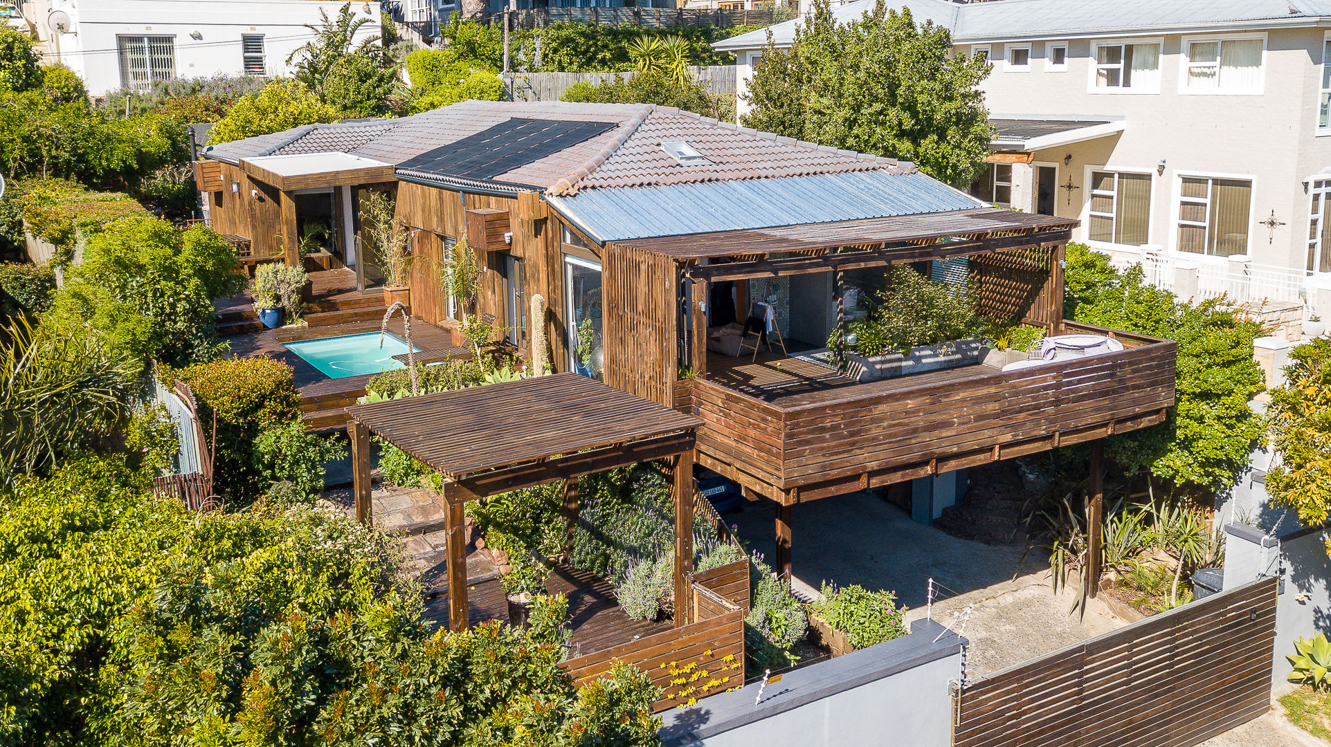 Aerial view of the timber clad home with its decks, pergolas and pool among the greenery